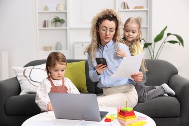 Photo of Work-family balance. Single mother with document using smartphone and her daughters indoors