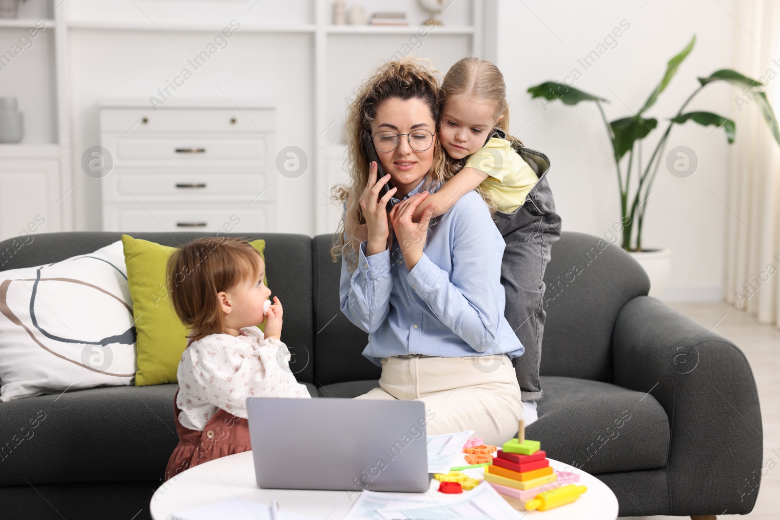 Photo of Work-family balance. Single mother talking on smartphone and her daughters at home