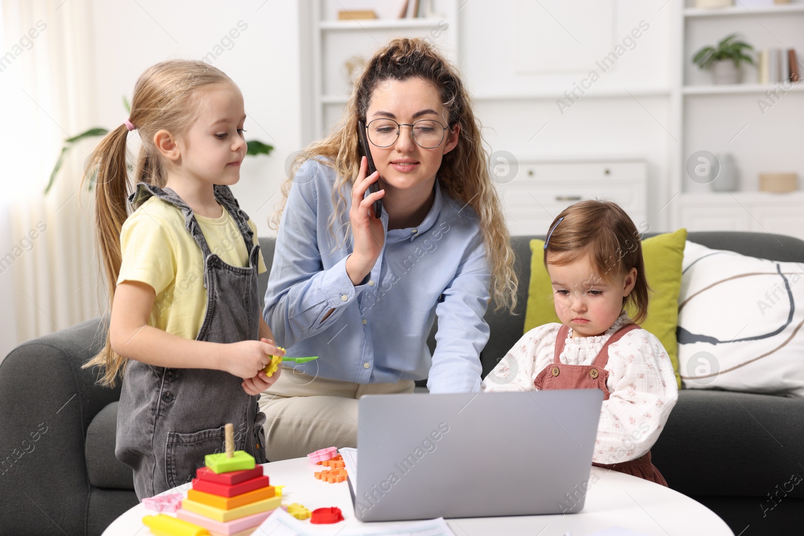 Photo of Work-family balance. Single mother talking on smartphone and her daughters at home