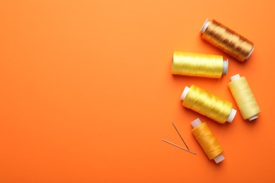 Spools of thread and needles on orange background, flat lay. Space for text