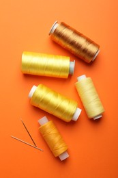 Photo of Spools of thread and needles on orange background, flat lay