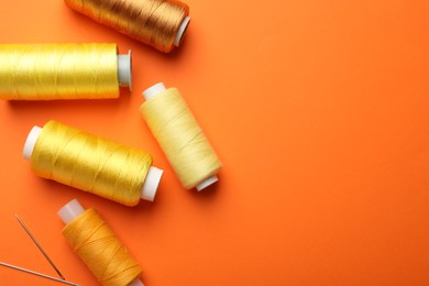 Spools of thread and needles on orange background, flat lay. Space for text