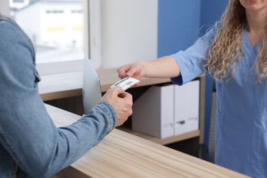 Photo of Patient giving medical insurance card to receptionist in clinic, closeup