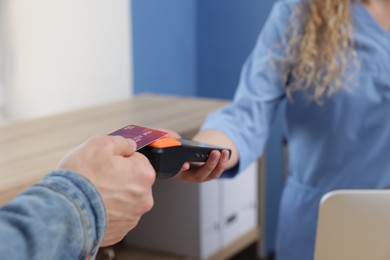 Receptionist taking payment from patient via terminal in clinic, closeup