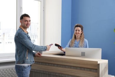 Photo of Smiling receptionist taking payment from patient via terminal in clinic