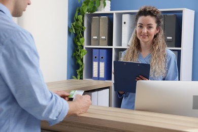 Photo of Smiling receptionist and patient with medical insurance card at counter in clinic