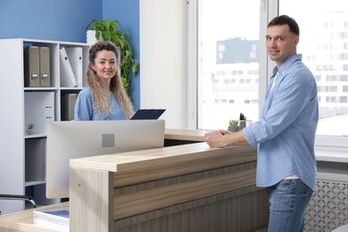 Photo of Smiling receptionist and patient with medical insurance card at counter in clinic