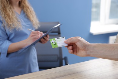 Photo of Patient with medical insurance card and receptionist at counter in clinic, closeup