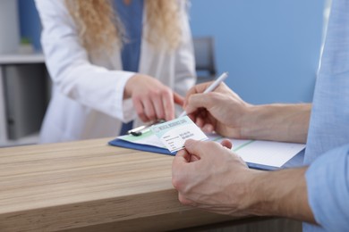 Photo of Patient with medical insurance card filling document and receptionist at counter in clinic, closeup