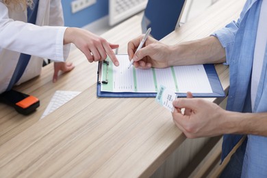 Photo of Patient with medical insurance card filling document and receptionist at counter in clinic, closeup