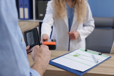 Photo of Receptionist taking payment from patient via terminal at counter in clinic, closeup