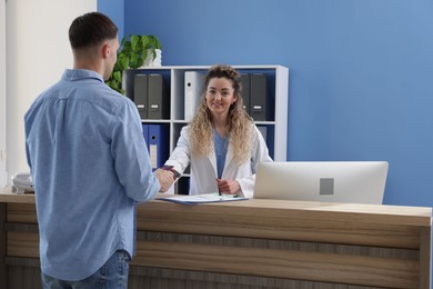 Photo of Smiling receptionist taking payment from patient via terminal at counter in clinic