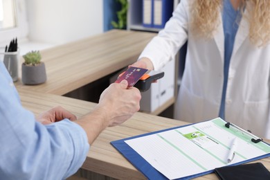 Photo of Receptionist taking payment from patient via terminal at counter in clinic, closeup