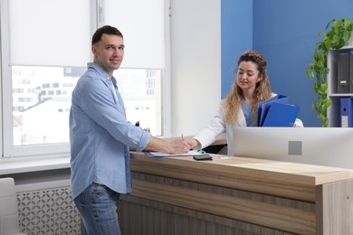 Smiling patient filling medical card and receptionist at counter in clinic