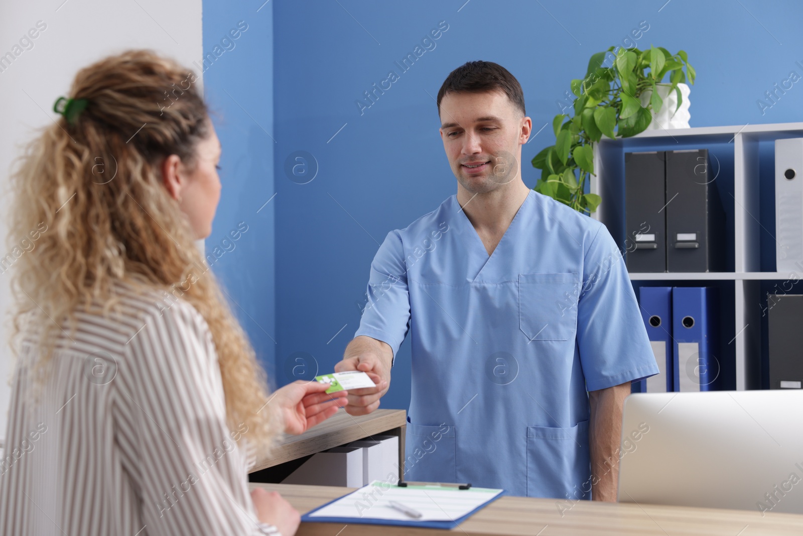 Photo of Patient giving medical insurance card to smiling receptionist in clinic