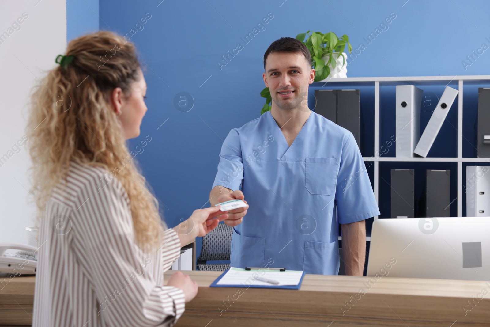 Photo of Patient giving medical insurance card to smiling receptionist in clinic