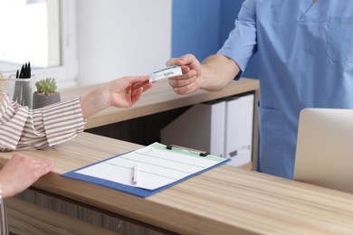 Photo of Patient giving medical insurance card to receptionist in clinic, closeup