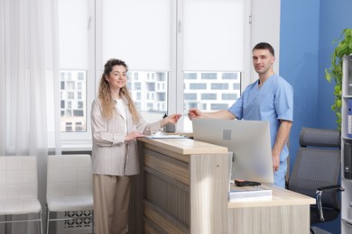 Photo of Patient giving medical insurance card to smiling receptionist in clinic