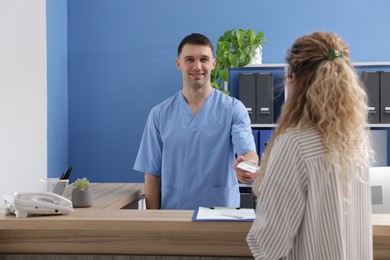 Photo of Patient giving medical insurance card to smiling receptionist in clinic