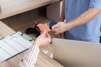 Photo of Receptionist taking payment from patient via terminal at counter in clinic, closeup