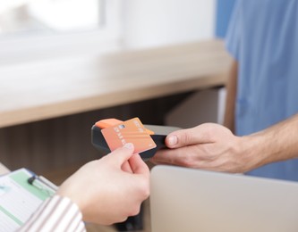 Receptionist taking payment from patient via terminal in clinic, closeup