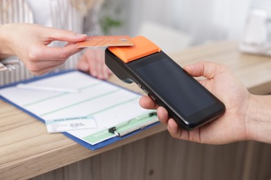 Photo of Receptionist taking payment from patient via terminal at counter in clinic, closeup