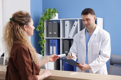 Photo of Patient giving medical insurance card to smiling receptionist in clinic