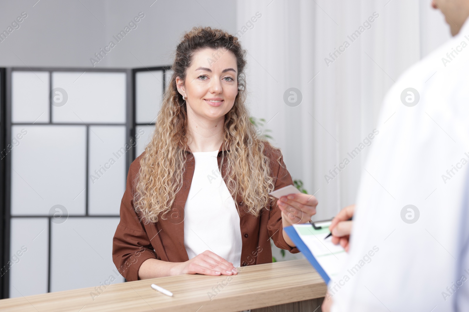 Photo of Smiling patient giving medical insurance card to receptionist in clinic