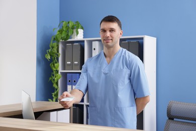 Smiling receptionist giving medical insurance card at counter in clinic