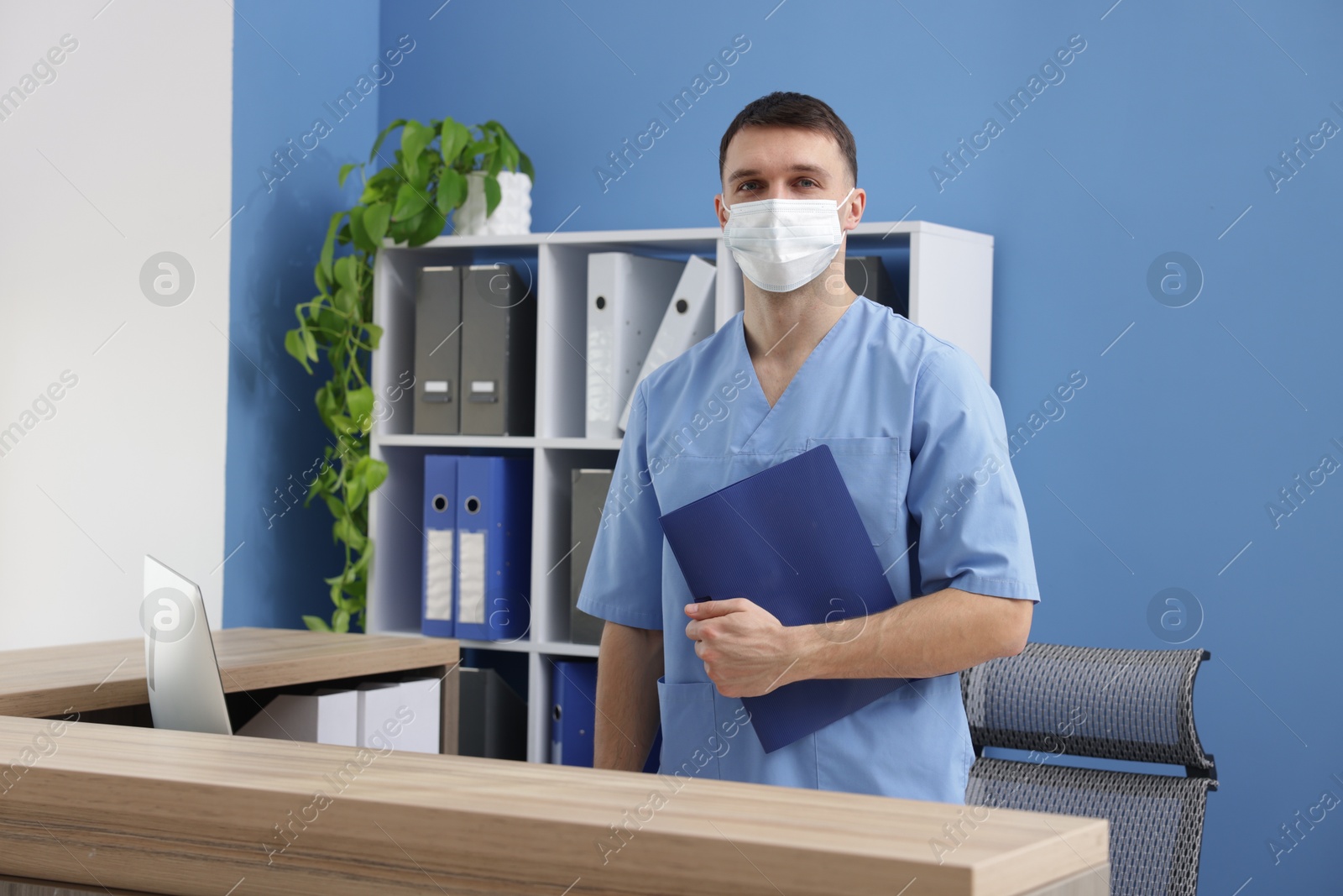 Photo of Receptionist in medical mask with clipboard at counter in clinic