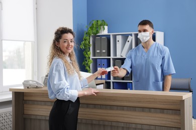 Photo of Smiling patient giving medical insurance card to receptionist at counter in clinic