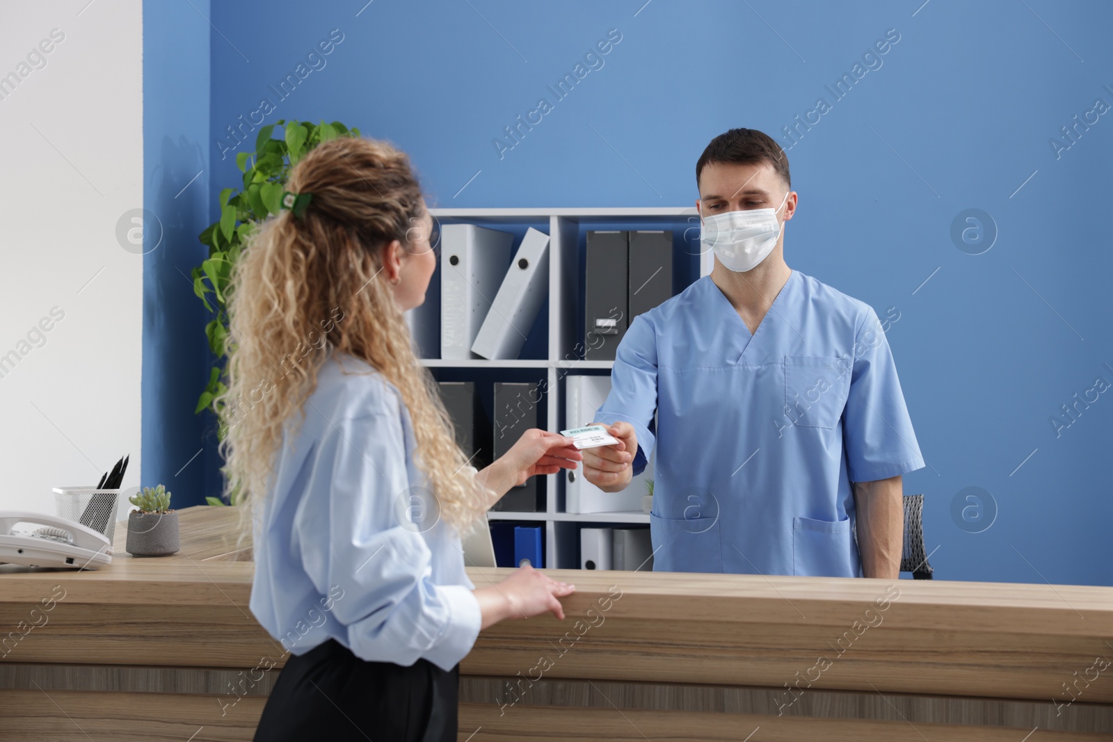 Photo of Patient giving medical insurance card to receptionist at counter in clinic