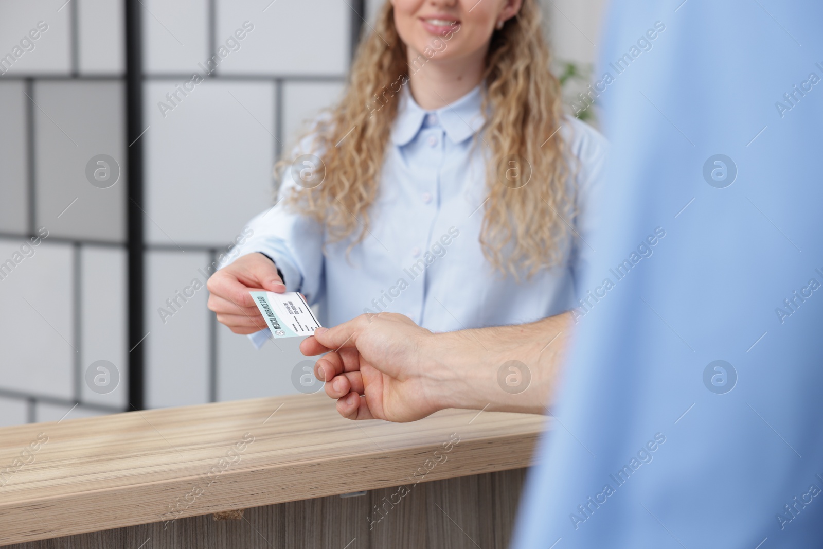 Photo of Smiling patient giving medical insurance card to receptionist in clinic, closeup