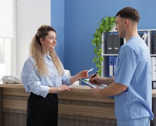 Smiling patient with medical insurance card and receptionist filling document in clinic