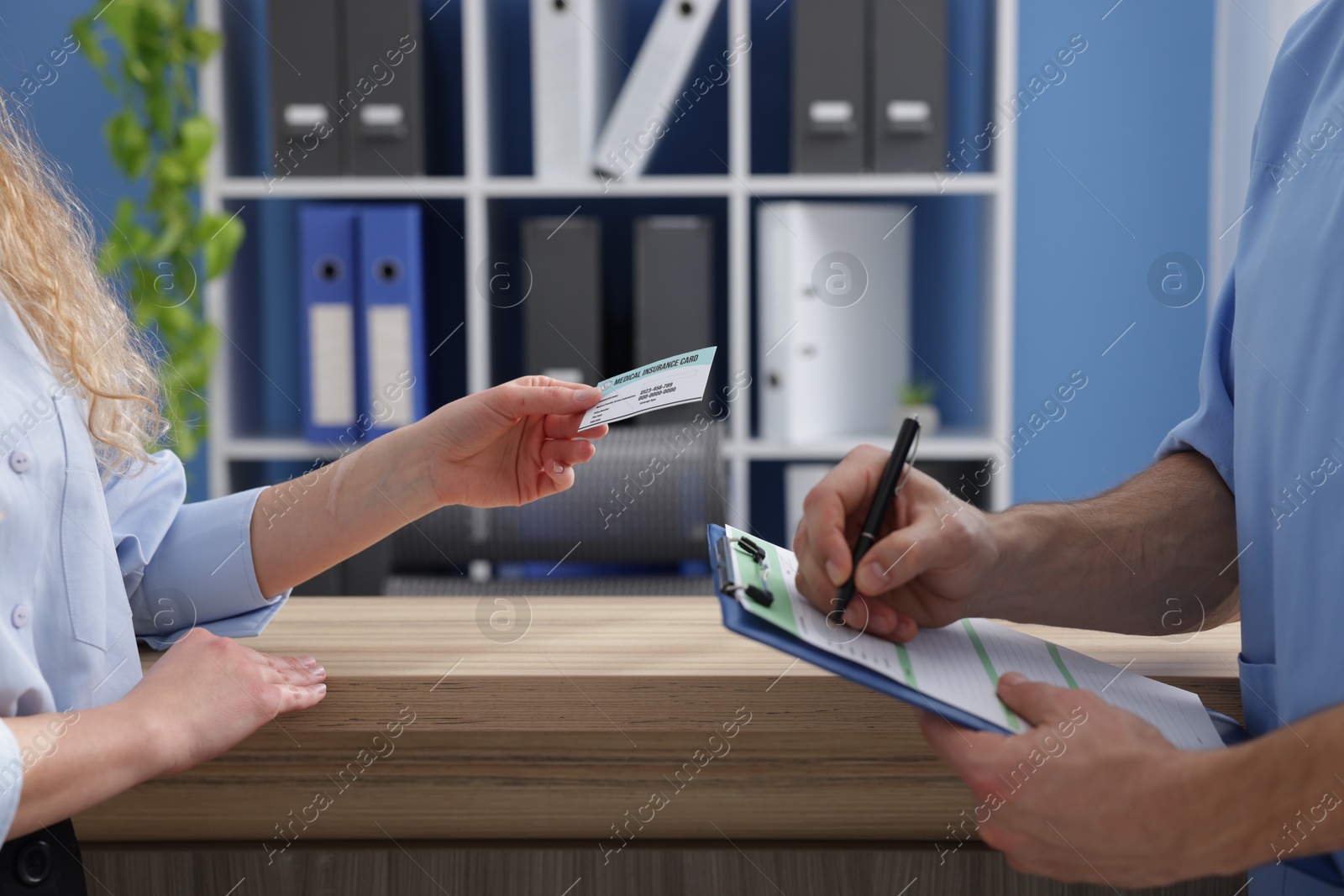 Photo of Patient with medical insurance card and receptionist filling document in clinic, closeup