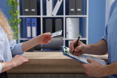 Patient with medical insurance card and receptionist filling document in clinic, closeup