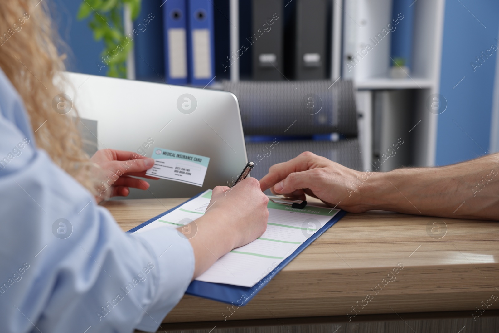 Photo of Patient with medical insurance card filling document and receptionist at counter in clinic, closeup