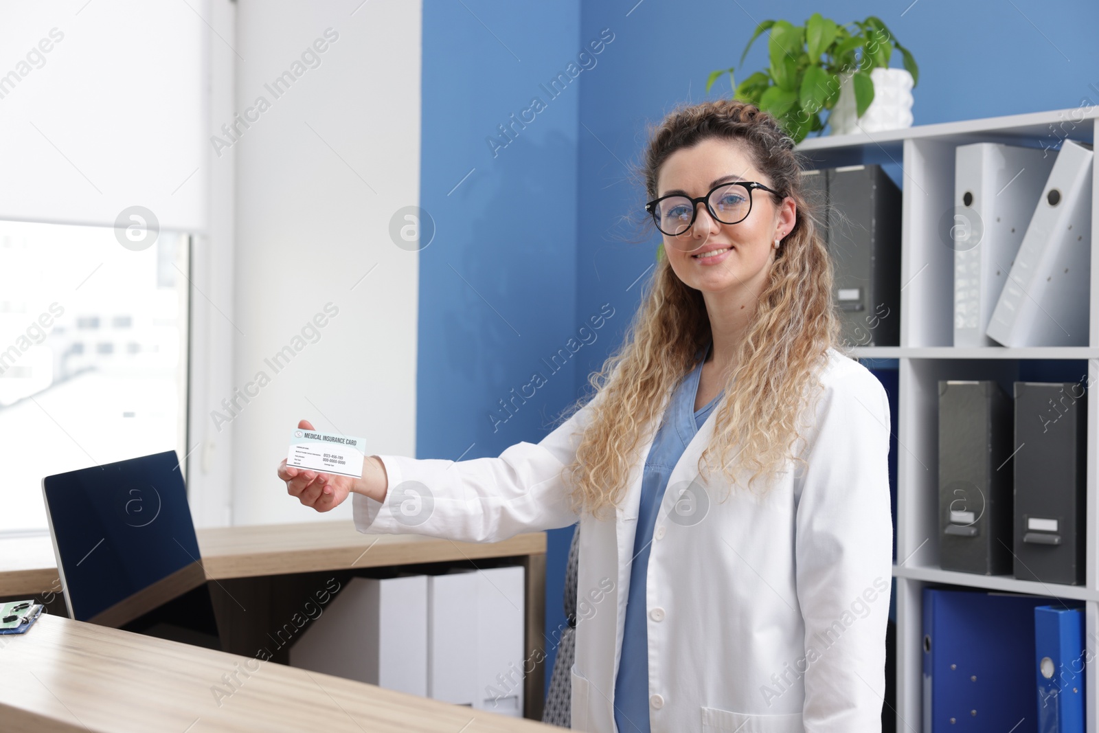 Photo of Smiling receptionist giving medical insurance card at counter in clinic