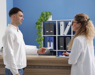 Smiling patient giving medical insurance card to receptionist in clinic