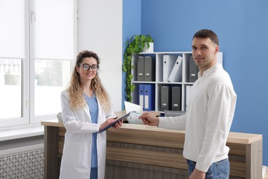 Photo of Smiling patient giving medical insurance card to receptionist in clinic