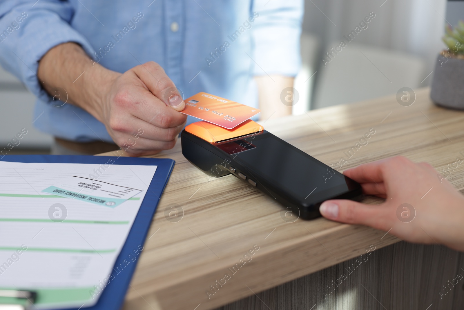 Photo of Patient paying with credit card via terminal which holding receptionist at counter in clinic, closeup