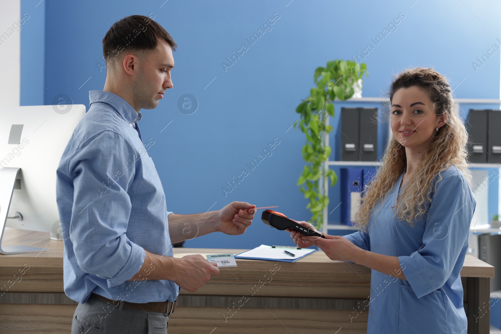 Photo of Smiling receptionist taking payment from patient with medical insurance card via terminal in clinic