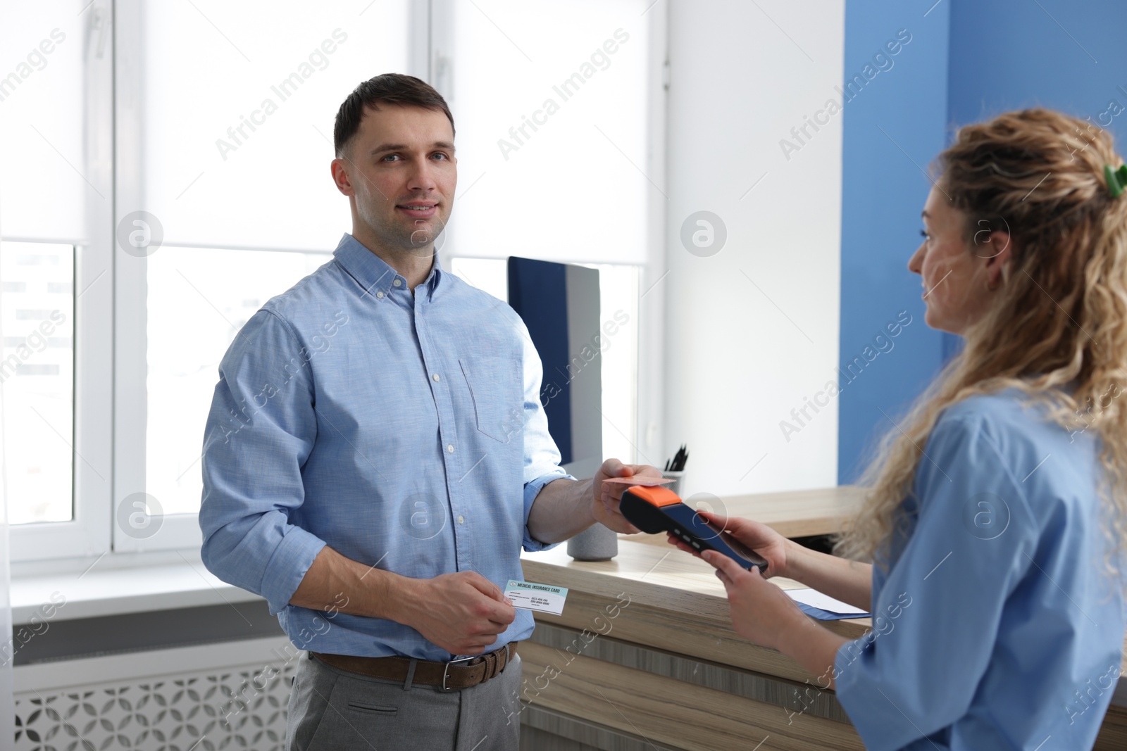 Photo of Receptionist taking payment from patient with medical insurance card via terminal in clinic