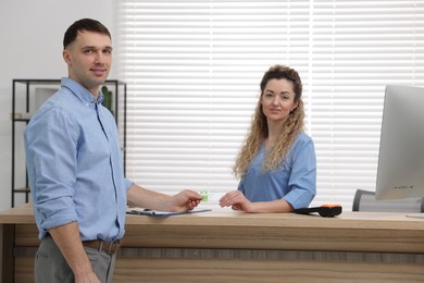 Photo of Smiling patient giving medical insurance card to receptionist at counter in clinic