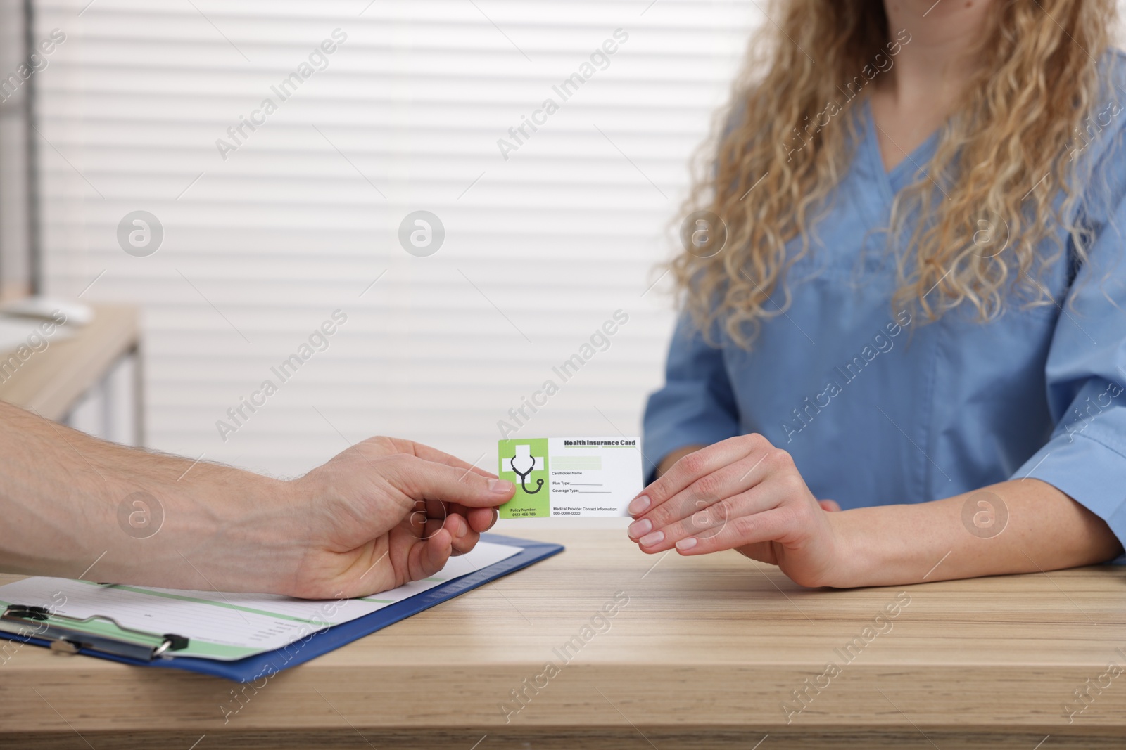 Photo of Patient giving medical insurance card to receptionist at wooden counter in clinic, closeup