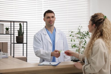 Patient giving medical insurance card to smiling receptionist at counter in clinic