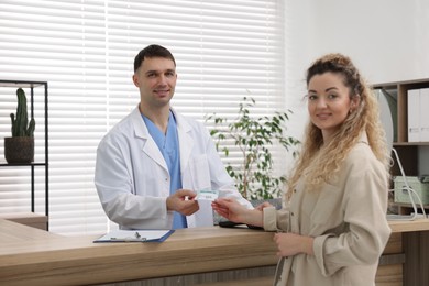 Photo of Patient giving medical insurance card to smiling receptionist at counter in clinic