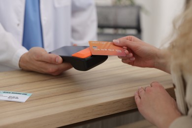 Photo of Receptionist taking payment from patient via terminal at wooden counter in clinic, closeup