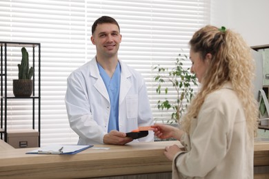 Smiling receptionist taking payment from patient via terminal in clinic