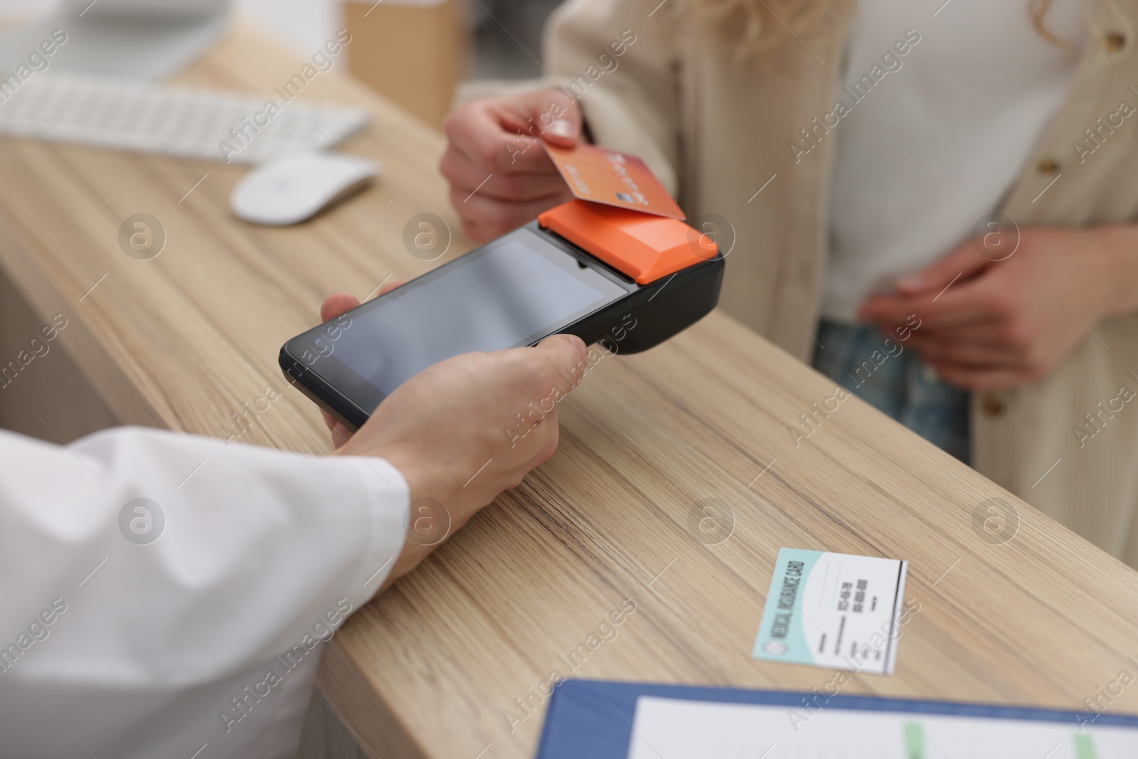 Photo of Receptionist taking payment from patient via terminal at wooden counter in clinic, closeup